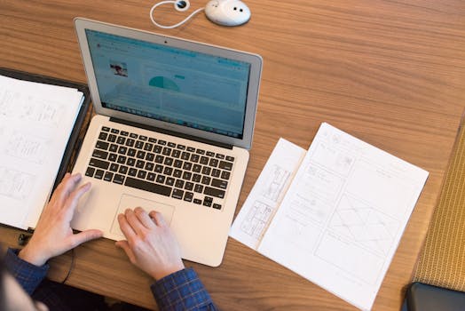 An overhead view of a person working on a laptop at a desk with documents and papers.